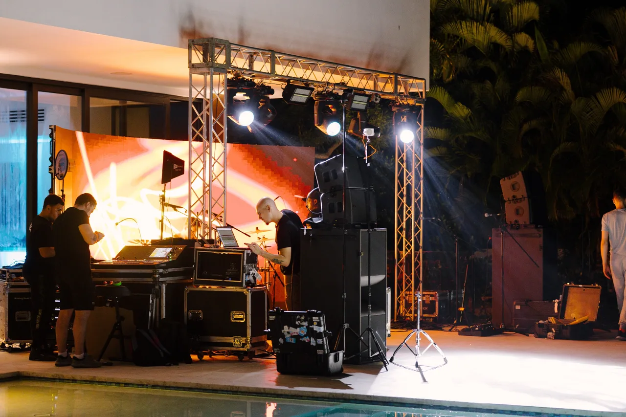 Crew setting up a truss, lights, sound and an LED screen beside a villa pool at night